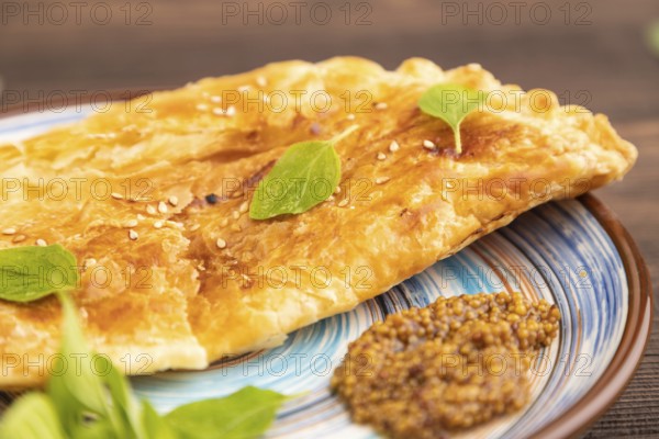 Fried homemade Khachapuri cake with cheese and meat, fried in pan. Traditional Georgian cuisine on brown wooden background. Side view, close up, selective focus