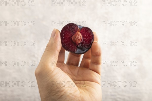 Purple Plum Cut in half with hand on gray concrete background. Side view, close up. healthy food, vegetable, minimalism