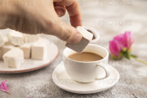 Coffee marshmallow with cup of coffee with hand on brown concrete background. side view, close up, selective focus