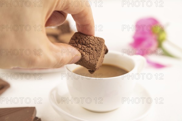 Chocolate marshmallow with cup of coffee with hand on white wooden background. side view, close up, selective focus