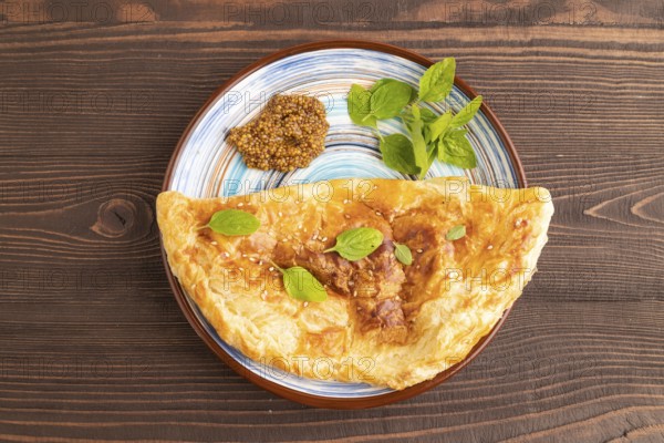 Fried homemade Khachapuri cake with cheese and meat, fried in pan. Traditional Georgian cuisine on brown wooden background. Side view, copy space