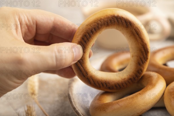 Homemade Ring Bagel with hand with cup of coffee on brown concrete background and linen textile. side view, close up, selective focus
