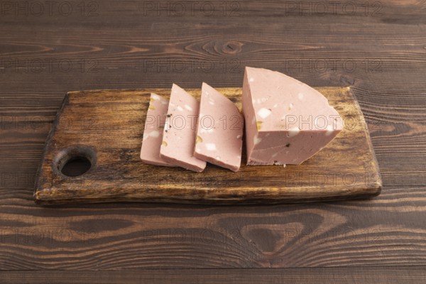 Mortadella sausage on wooden cutting board with pepper and herbs on brown wooden background. Side view, close up