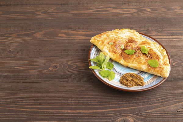 Fried homemade Khachapuri cake with cheese and meat, fried in pan. Traditional Georgian cuisine on brown wooden background. Side view, copy space