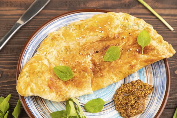 Fried homemade Khachapuri cake with cheese and meat, fried in pan. Traditional Georgian cuisine on brown wooden background. Side view, close up, selective focus