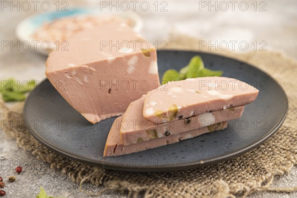 Mortadella sausage on plate with pepper and herbs on brown concrete background and linen textile. Side view, close up, selective focus
