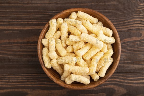 Corn flakes sticks with caramel in wooden bowl on brown wooden background. Top view, flat lay, copy space