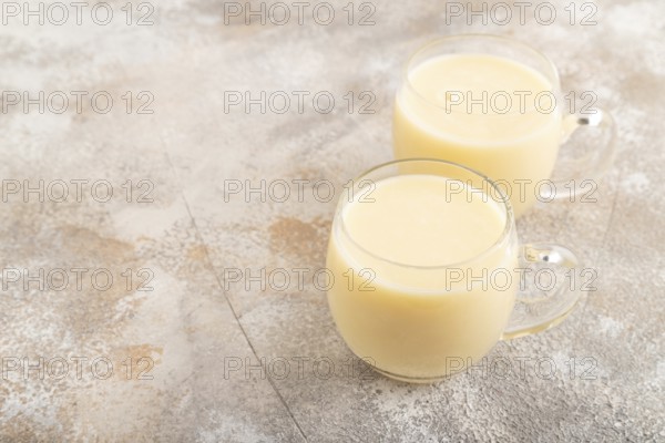 Organic non dairy banana and soy milk in glass on brown concrete background. Vegan healthy food concept, side view, copy space