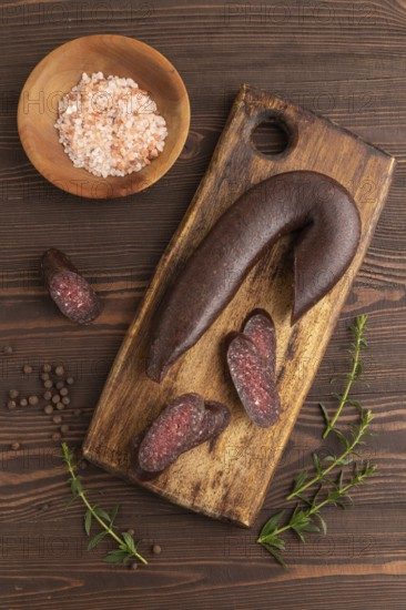 Sujuk sausage on wooden cutting board with pepper and herbs on brown wooden background. Top view, flat lay, copy space
