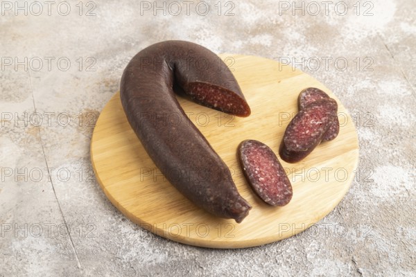 Sujuk sausage on wooden cutting board with pepper and herbs on brown concrete background. Side view, close up