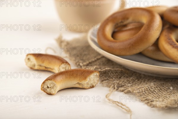 Homemade Ring Bagel with cup of coffee on white wooden background and linen textile. side view, close up, selective focus