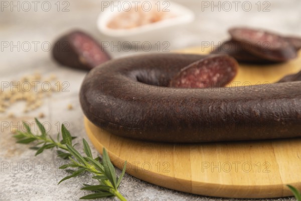 Sujuk sausage on wooden cutting board with pepper and herbs on brown concrete background. Side view, close up, selective focus