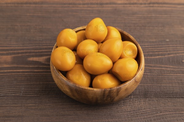 Pile of Smoked Quail eggs in bowl on a brown wooden background. side view, close up