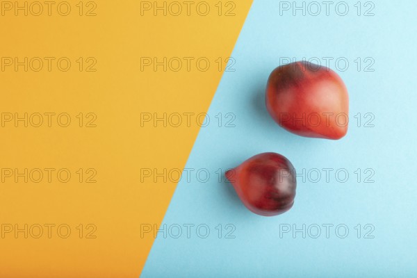 Red Heart shape tomatoes on blue and orange pastel paper background. Top view, copy space, flat lay. healthy food, vegetable, minimalism