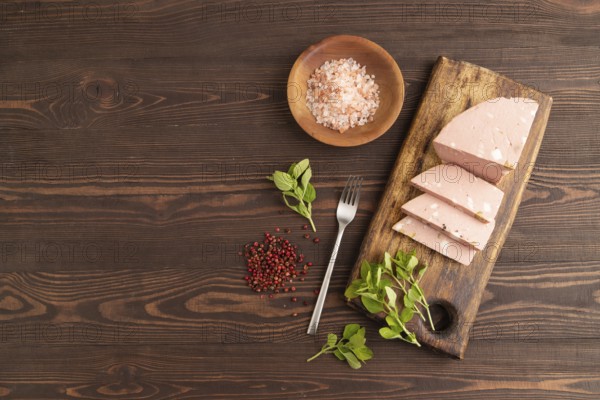 Mortadella sausage on wooden cutting board with pepper and herbs on brown wooden background. Top view, flat lay, copy space
