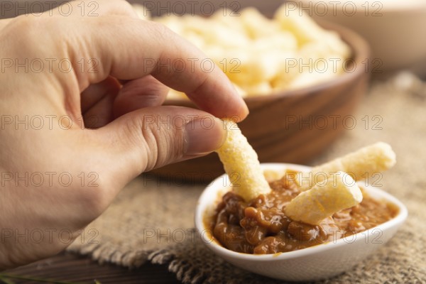 Corn flakes sticks with caramel in wooden bowl with hand on brown wooden background and linen textile. Side view, close up, selective focus