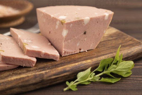 Mortadella sausage on wooden cutting board with pepper and herbs on brown wooden background. Side view, close up, selective focus
