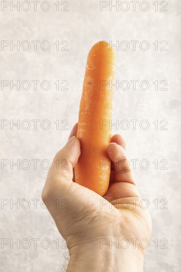 Orange Carrot with hand on gray concrete background. Top view, close up, flat lay. healthy food, vegetable, minimalism