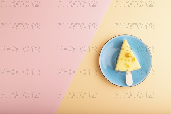 Yellow Cake pop with sprinkles on blue ceramic plate on pink and orange pastel paper background, top view, flat lay, copy space, minimalism