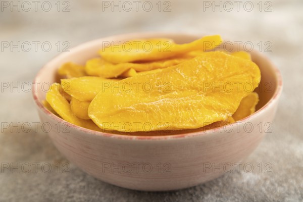 Dried Mango in ceramic bowl on brown concrete background. Side view, close up, selective focus. healthy food, minimalism