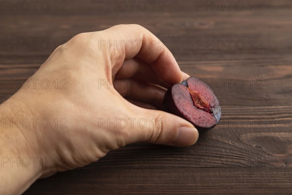 Purple Plum Cut in half with hand on brown wooden background. Side view, close up. healthy food, vegetable, minimalism