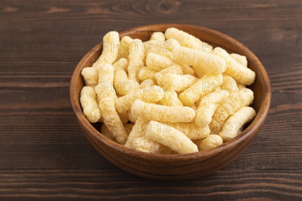 Corn flakes sticks with caramel in wooden bowl on brown wooden background. side view, close up