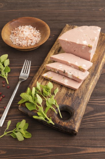 Mortadella sausage on wooden cutting board with pepper and herbs on brown wooden background. Side view, close up