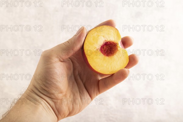 Peach Cut in half with hand on brown concrete background. Side view, copy space. healthy food, vegetable, minimalism