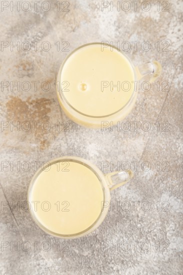 Organic non dairy banana and soy milk in glass on brown concrete background. Vegan healthy food concept, flat lay, top view, close up