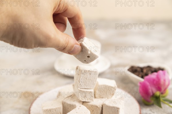 Coffee marshmallow with cup of coffee with hand on brown concrete background. side view, close up, selective focus