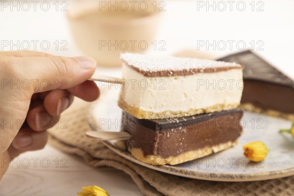 Chocolate and Vanilla Cake pops Marshmallow with hand with cup of coffee on white wooden background and beige linen textile. side view, close up, selective focus hold