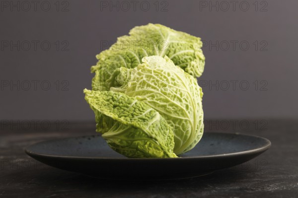 Green lettuce on blue plate on black concrete background. Side view, copy space. healthy food, vegetable, minimalism, low key