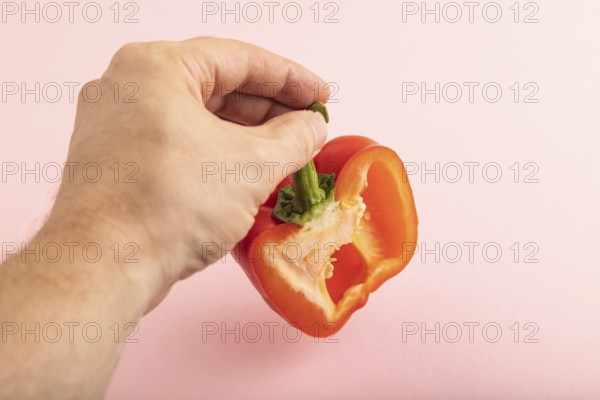 Hand holding sliced Red Cutted pepper on pink pastel background. Side view, copy space. Tropical, healthy food, vegetable, minimalism