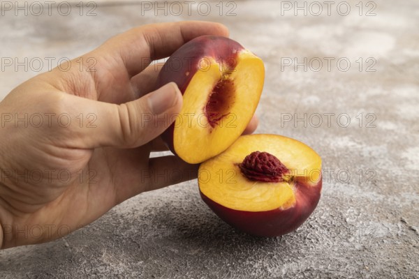 Peach Cut in half with hand on brown concrete background. Side view, copy space. healthy food, vegetable, minimalism