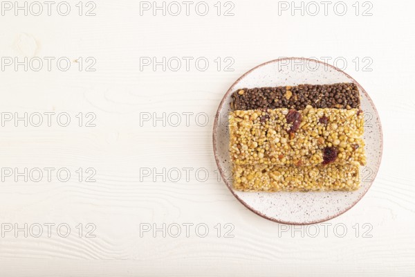 Granola bars with caramel, nuts, flakes in ceramic plate on white wooden background. Top view, flat lay, copy space