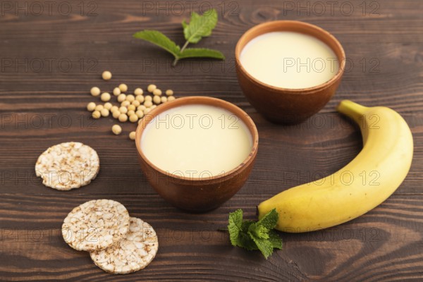 Organic non dairy banana and soy milk in clay cup on brown wooden background. Vegan healthy food concept, flat lay, side view, close up