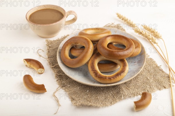 Homemade Ring Bagel with cup of coffee on white wooden background and linen textile. side view, close up