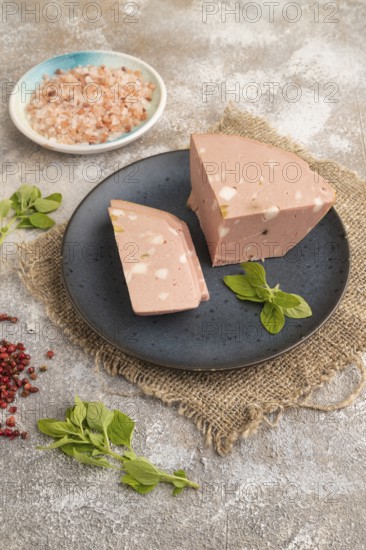 Mortadella sausage on plate with pepper and herbs on brown concrete background and linen textile. Side view, close up