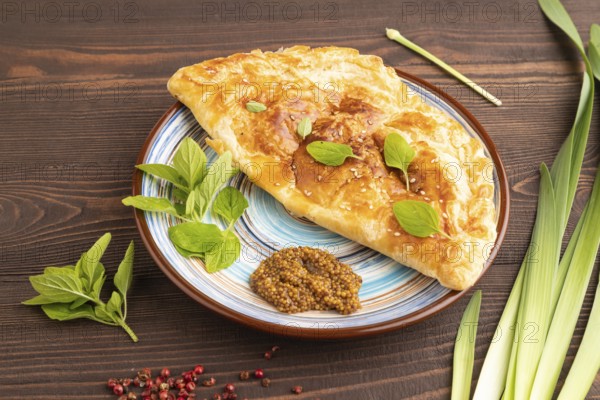 Fried homemade Khachapuri cake with cheese and meat, fried in pan. Traditional Georgian cuisine on brown wooden background. Side view, close up
