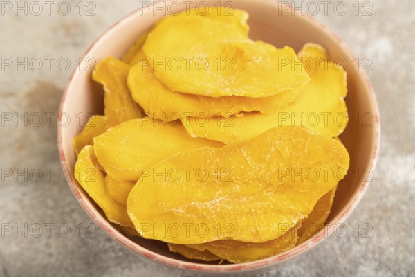 Dried Mango in ceramic bowl on brown concrete background. Side view, close up, selective focus. healthy food, minimalism