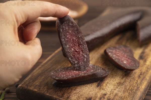 Sujuk sausage with hand on wooden cutting board with pepper and herbs on brown wooden background. Side view, close up, selective focus