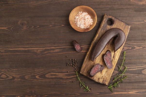 Sujuk sausage on wooden cutting board with pepper and herbs on brown wooden background. Top view, flat lay, copy space