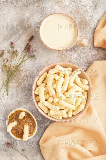 Corn flakes sticks with caramel in ceramic bowl on gray concrete background and orange linen textile. Top view, flat lay, close up