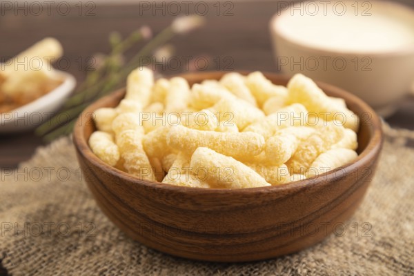 Corn flakes sticks with caramel in wooden bowl on brown wooden background and linen textile. Side view, close up, selective focus