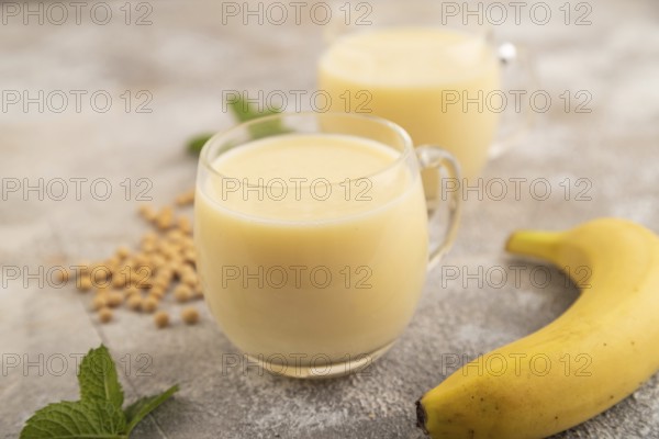 Organic non dairy banana and soy milk in glass on brown concrete background. Vegan healthy food concept, side view, close up, selective focus