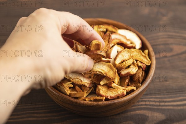 Dried Apples in wooden bowl with hand on brown wooden background. Side view, close up, healthy food, minimalism. sweet, selective focus