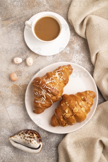 Croissant on white plate on brown concrete background and linen textile, cup of coffee, top view, flat lay, close up