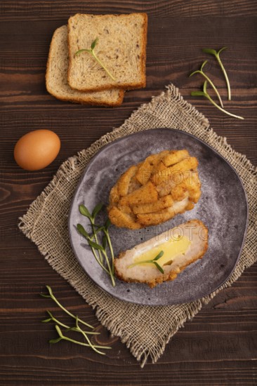 Chicken Schnitzel on gray plate with microgreen on brown wooden background and linen textile. top view, flat lay, close up