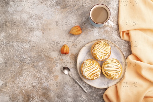 French lemon tart with meringue on brown concrete background, cup of coffee, orange linen textile, top view, flat lay, copy space
