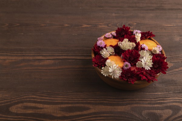Wooden bowl with carrot slices and red Chrysanthemum flowers, Astrantia flowers, flower salad on brown wooden background, side view. copy space, minimalism